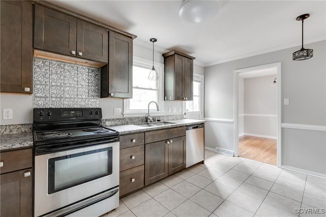 Kitchen with appliances with stainless steel finishes, dark brown cabinetry, crown molding, hanging light fixtures, and light tile patterned floors | Image 9