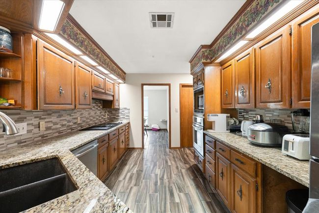 Kitchen with a sink, appliances with stainless steel finishes, open shelves, decorative backsplash, and light stone counters | Image 14