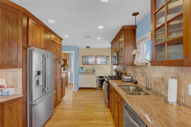 Kitchen with light wood-type flooring, hanging light fixtures, light stone countertops, sink, and appliances with stainless steel finishes | Image 15
