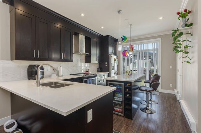 Kitchen with wall chimney range hood, stainless steel appliances, a sink, baseboards, and a breakfast bar area | Image 19