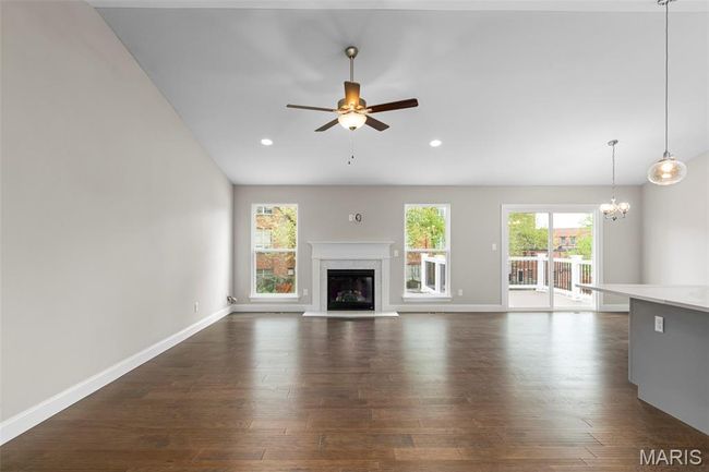 Unfurnished living room featuring dark wood-style floors, ceiling fan, a glass covered fireplace, a chandelier, and baseboards | Image 14