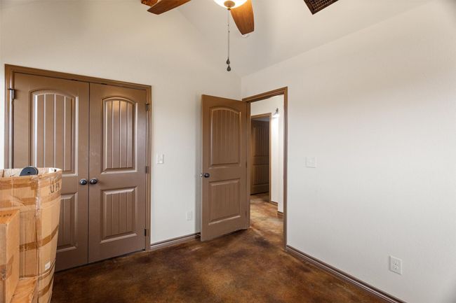 Bedroom featuring a ceiling fan, concrete flooring, baseboards, high vaulted ceiling, and a closet | Image 6