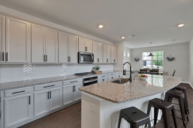 Kitchen with a kitchen bar, dark wood-style flooring, stainless steel appliances, a sink, and light stone countertops | Image 9