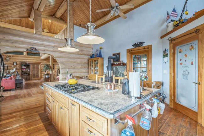 Kitchen with wood ceiling with exposed beams, log walls, gas stovetop, wood-type flooring, and arched walkways | Image 30