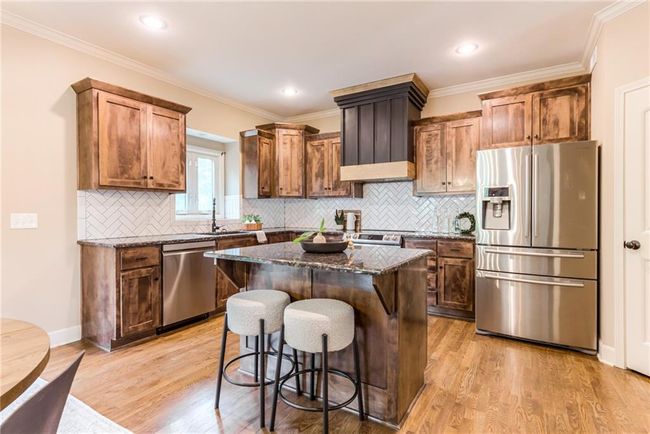 Kitchen featuring stainless steel appliances, a kitchen breakfast bar, dark stone counters, light wood-type flooring, and a center island | Image 11