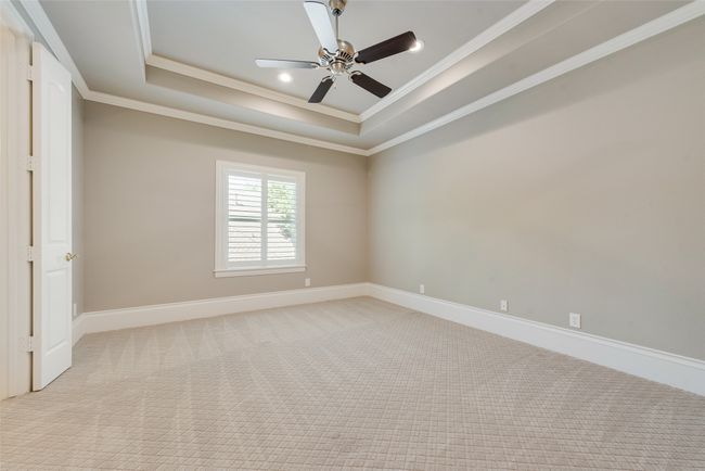 Empty room with a raised ceiling, ceiling fan, light colored carpet, and ornamental molding | Image 28