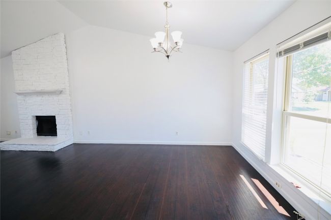 Unfurnished living room featuring vaulted ceiling, a chandelier, dark wood-style floors, and a stone fireplace | Image 12
