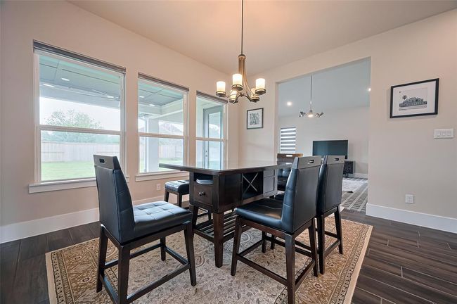 This dining area features large windows with backyard views, a modern chandelier, and an open layout leading to a living space. The dark wood floors and furniture contrast nicely with the neutral walls, creating a cozy yet elegant atmosphere. | Image 18
