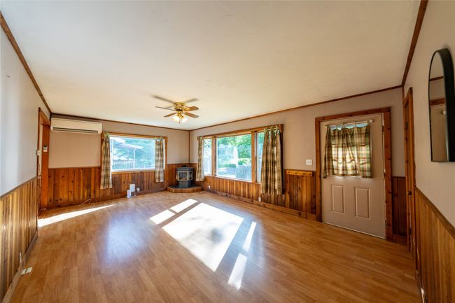Unfurnished living room with a wainscoted wall, a wall unit AC, a wood stove, wood walls, and wood finished floors | Image 5