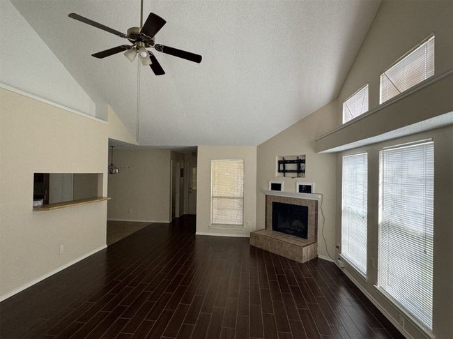 Unfurnished living room featuring high vaulted ceiling, dark wood-type flooring, ceiling fan, and a fireplace | Image 4