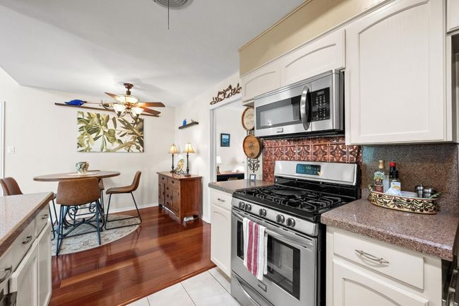 Kitchen with white cabinets, appliances with stainless steel finishes, a ceiling fan, wood finished floors, and backsplash | Image 14