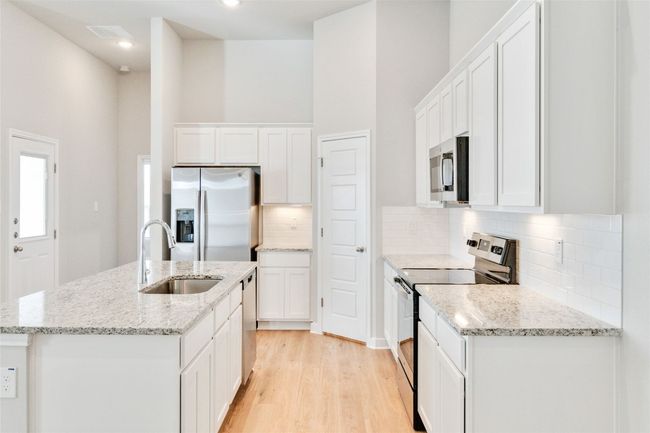 Kitchen with a center island with sink, stainless steel appliances, white cabinets, a sink, and light wood-type flooring | Image 15