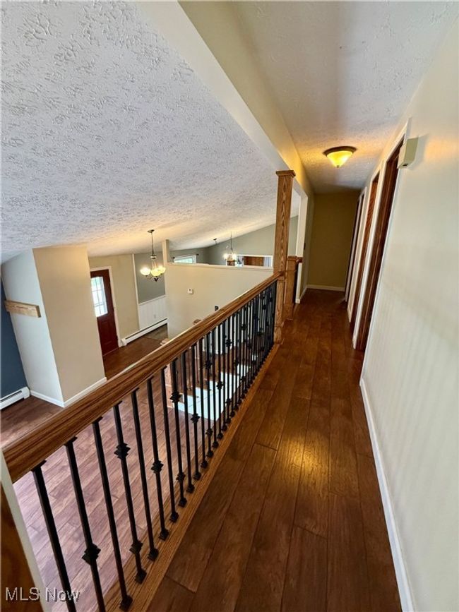 Corridor with a textured ceiling, an inviting chandelier, baseboards, and dark wood finished floors | Image 33