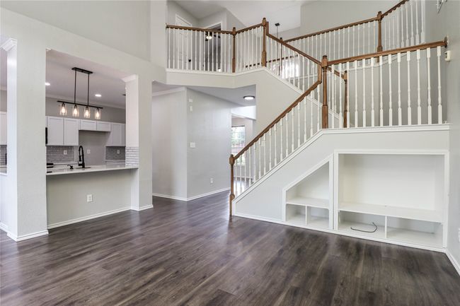 Unfurnished living room with a sink, dark wood finished floors, baseboards, a high ceiling, and stairway | Image 6