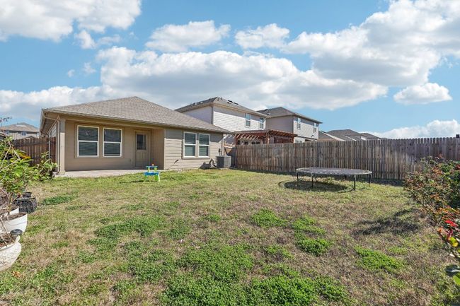 Rear view of house featuring a trampoline, central AC, a lawn, a fenced backyard, and a patio | Image 22