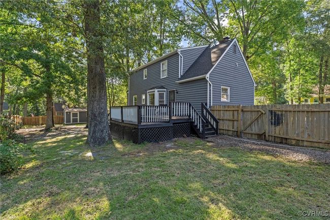 Back of house featuring a deck, a storage unit, a fenced backyard, a shingled roof, and view of scattered trees | Image 42