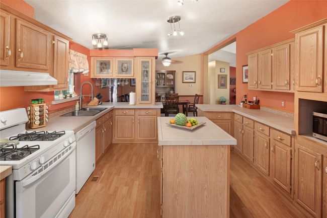 Kitchen featuring white appliances, under cabinet range hood, light countertops, light brown cabinetry, and light wood-type flooring | Image 17