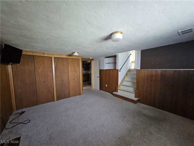 Finished basement with wooden walls, visible vents, carpet floors, a textured ceiling, and stairs | Image 9