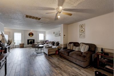 Living room with wood look tile flooring, a brick fireplace, a textured ceiling, and ceiling fan | Image 2