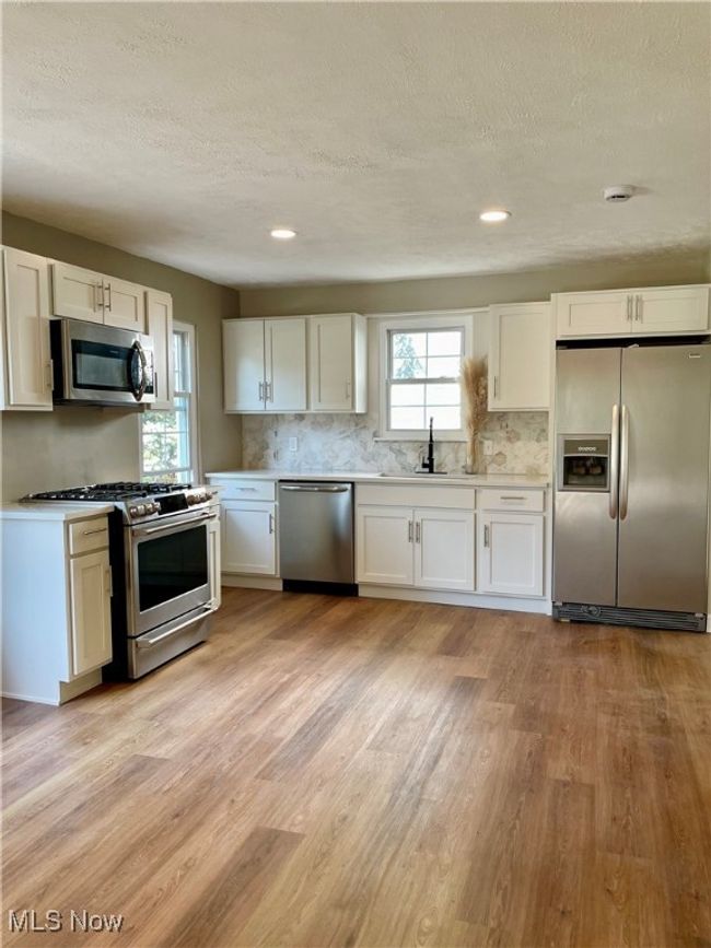 Kitchen featuring appliances with stainless steel finishes, a textured ceiling, light wood finished floors, white cabinetry, and decorative backsplash | Image 6