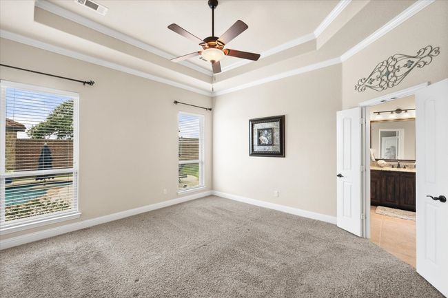 Primary bedroom with a raised ceiling, crown molding, carpet, and a ceiling fan | Image 11