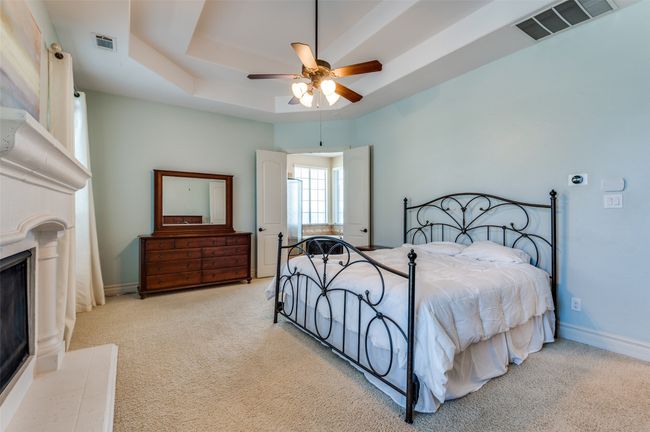 Carpeted bedroom featuring visible vents, a fireplace with raised hearth, a raised ceiling, and baseboards | Image 25