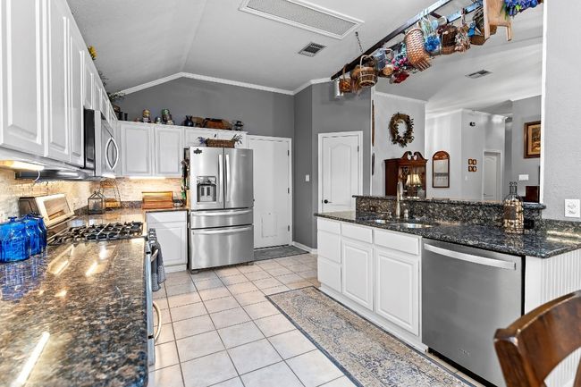 Kitchen featuring appliances with stainless steel finishes, white cabinetry, lofted ceiling, dark stone countertops, and light tile patterned floors | Image 15
