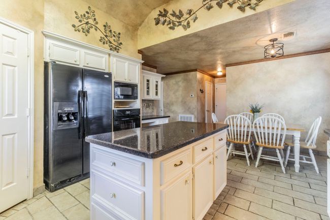 Kitchen with black appliances, white cabinets, a kitchen island, dark stone counters, and vaulted ceiling | Image 6