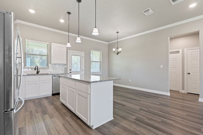 Kitchen featuring appliances with stainless steel finishes, dark wood-type flooring, a kitchen island, crown molding, and white cabinetry | Image 16