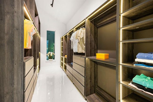 Step into a boutique-style walk-in closet designed for both elegance and functionality. Custom wood cabinetry with soft-close drawers, abundant shelving, and integrated LED lighting provide a luxurious backdrop for organizing your wardrobe in style. A sleek, modern layout makes this space as beautiful as it is practical. | Image 25