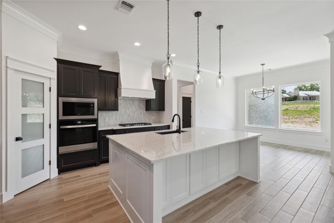 Kitchen featuring sink, backsplash, custom exhaust hood, a kitchen island with sink, and stainless steel appliances | Image 13