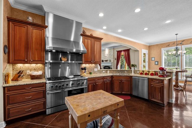 Thermador 48” six-burner range beneath a sleek stainless steel hood, set against a granite backsplash with a butcher-block prep island at center. Double-oven for ease of meal preparation for those big functions. | Image 17