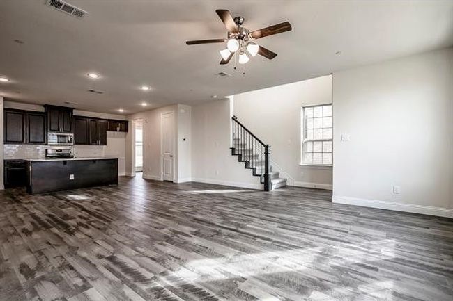 Unfurnished living room featuring visible vents, baseboards, dark wood-style flooring, ceiling fan, and stairs | Image 7