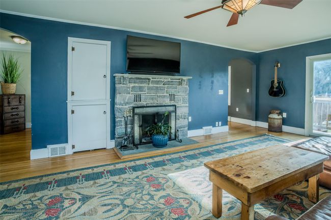 Living room featuring ceiling fan, a stone fireplace, wood-type flooring, and crown molding | Image 7
