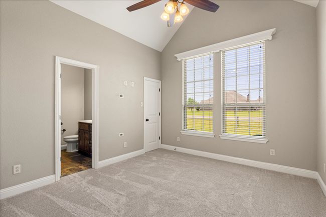 Unfurnished bedroom featuring carpet floors, ensuite bath, ceiling fan, and high vaulted ceiling | Image 7