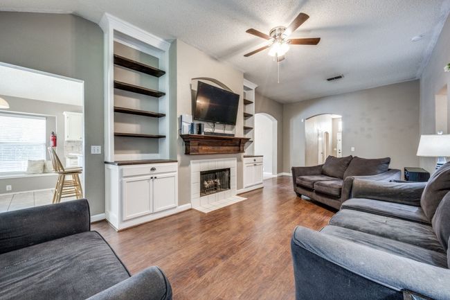 Living area with arched walkways, ceiling fan, wood finished floors, a fireplace, and a textured ceiling | Image 5