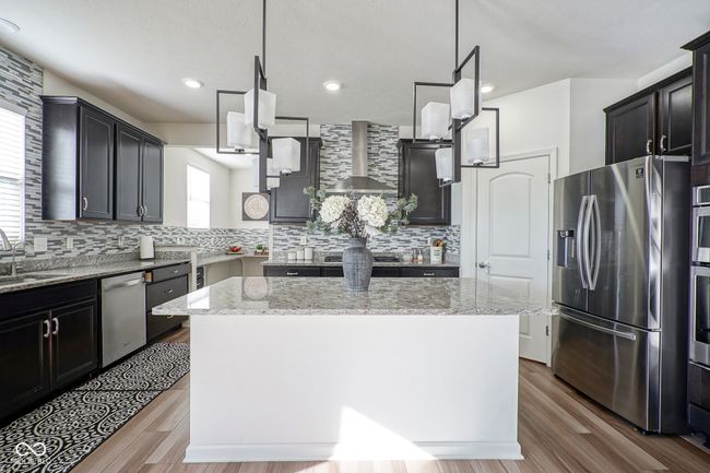 kitchen with wall chimney exhaust hood, a kitchen island, appliances with stainless steel finishes, light stone counters, and backsplash | Image 18