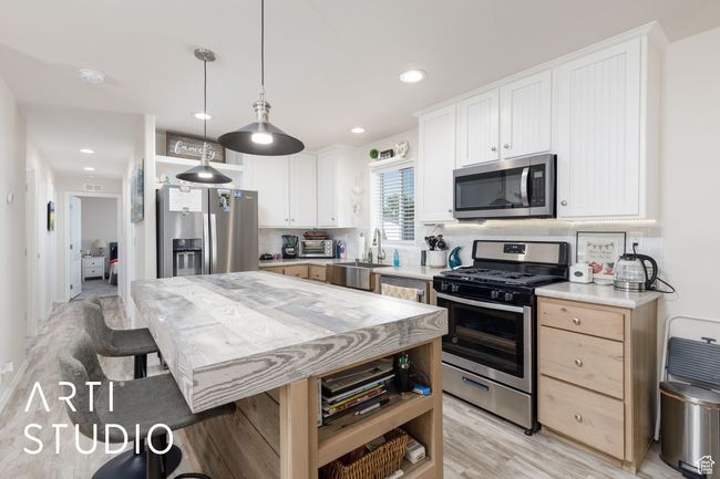 Kitchen with stainless steel appliances, light countertops, light wood finished floors, hanging light fixtures, and white cabinets | Image 11
