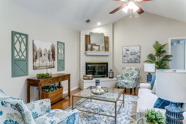 Living area with vaulted ceiling, a ceiling fan, wood finished floors, and a fireplace | Image 9