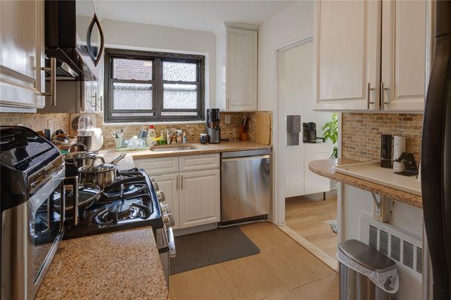 Kitchen with appliances with stainless steel finishes, a sink, backsplash, and white cabinetry | Image 6