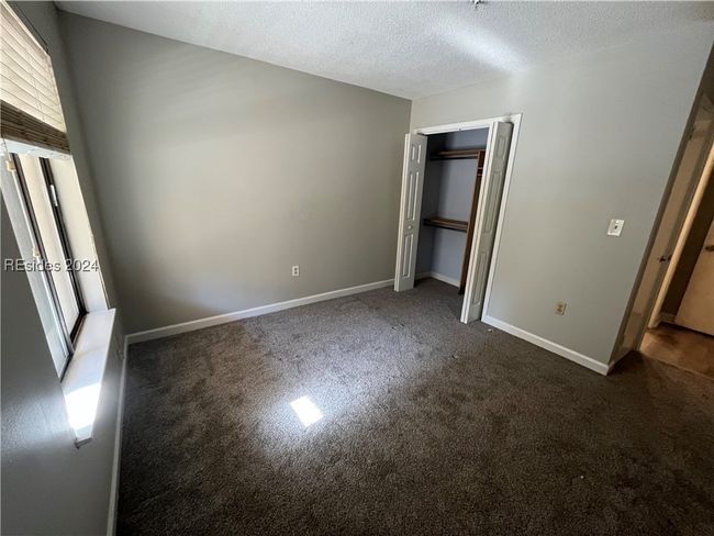 Unfurnished bedroom with a closet, a textured ceiling, and dark carpet | Image 8