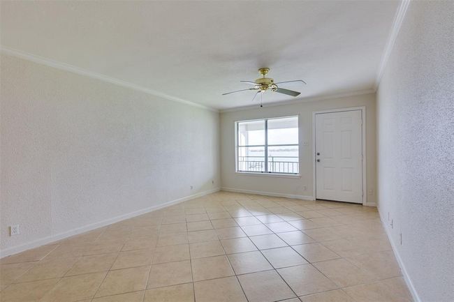 This room features light-colored tile flooring, neutral walls, and a ceiling fan. It includes a window and a door, allowing natural light to brighten the space, offering a view of the outdoors. | Image 4