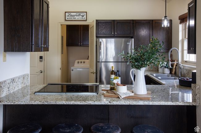 Kitchen with freestanding refrigerator, washer / clothes dryer, dark brown cabinets, a sink, and a peninsula | Image 5