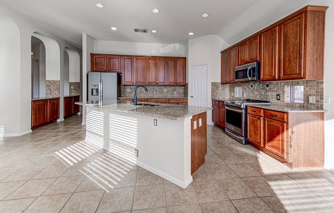 Kitchen featuring a sink, light stone counters, appliances with stainless steel finishes, and a center island with sink | Image 14