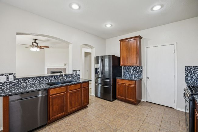 Kitchen featuring appliances with stainless steel finishes, a ceiling fan, tasteful backsplash, arched walkways, and dark stone countertops | Image 12