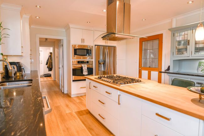 Kitchen featuring stainless steel appliances, a sink, island exhaust hood, crown molding, and butcher block counters | Image 13