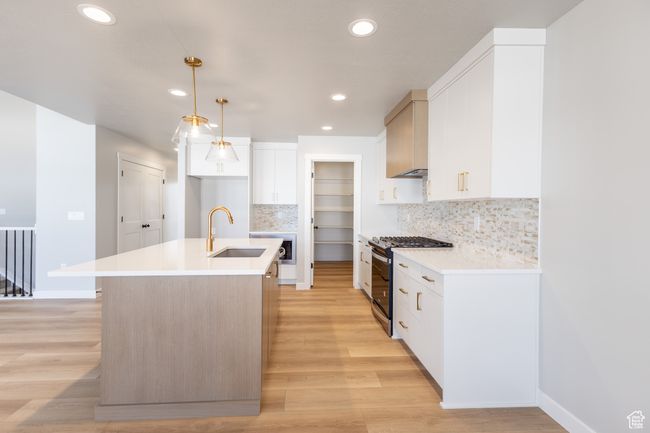 Kitchen featuring a sink, stainless steel range with gas cooktop, light wood finished floors, a kitchen island with sink, and tasteful backsplash | Image 10