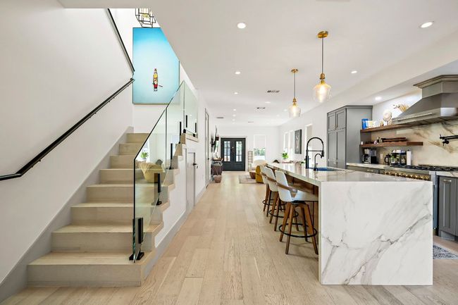 Kitchen with wall chimney exhaust hood, a sink, stainless steel gas range, gray cabinetry, and light stone countertops | Image 22