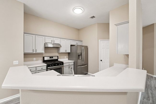 Kitchen with stainless steel appliances, light countertops, light wood-type flooring, and a peninsula | Image 9