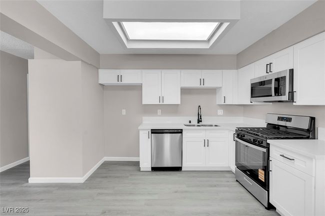 Kitchen with a sink, stainless steel appliances, light countertops, white cabinets, and baseboards | Image 13